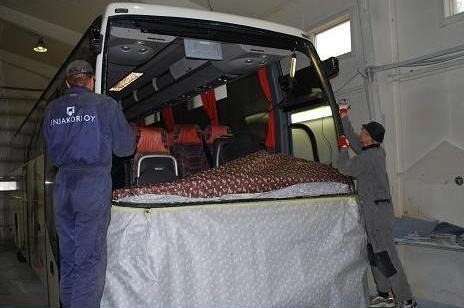 Asentajat vaihtamassa bussin tuulilasia korjaamohallissa
